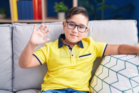 Photo for Young hispanic kid sitting on the sofa at home looking positive and happy standing and smiling with a confident smile showing teeth - Royalty Free Image