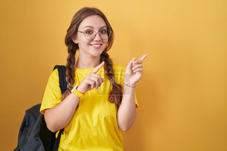 Photo for Young caucasian woman wearing student backpack over yellow background smiling and looking at the camera pointing with two hands and fingers to the side. - Royalty Free Image