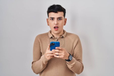 Photo for Non binary person using smartphone typing message in shock face, looking skeptical and sarcastic, surprised with open mouth - Royalty Free Image
