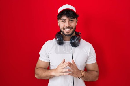 Photo for Hispanic man with beard wearing gamer hat and headphones hands together and fingers crossed smiling relaxed and cheerful. success and optimistic - Royalty Free Image