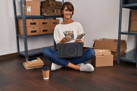 Foto de Joven mujer hispana hermosa comercio electrónico trabajador de negocios contando dólares utilizando el ordenador portátil en la oficina - Imagen libre de derechos