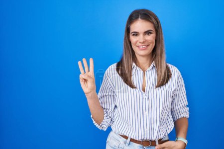 Photo for Hispanic young woman standing over blue background showing and pointing up with fingers number three while smiling confident and happy. - Royalty Free Image