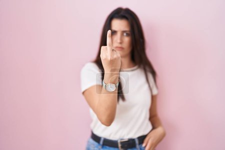 Foto de Young brunette woman standing over pink background showing middle finger, impolite and rude fuck off expression - Imagen libre de derechos