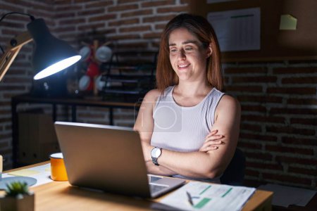Téléchargez les photos : Femme brune travaillant au bureau la nuit heureux visage souriant avec les bras croisés en regardant la caméra. personne positive. - en image libre de droit