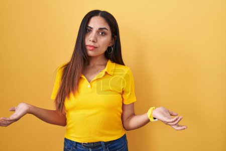 Téléchargez les photos : Jeune femme arabe debout sur fond jaune désemparé et confondu avec les bras ouverts, aucune idée concept. - en image libre de droit
