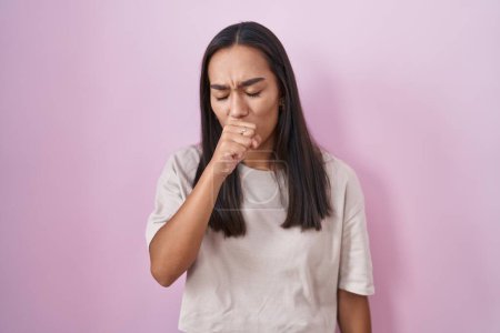 Foto de Mujer hispana joven parada sobre un fondo rosado sintiéndose mal y tosiendo como síntoma de resfriado o bronquitis. concepto de atención sanitaria. - Imagen libre de derechos