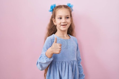 Téléchargez les photos : Jeune fille debout sur fond rose souriant heureux et positif, pouce levé faire excellent et signe d'approbation - en image libre de droit
