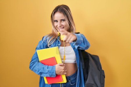 Photo for Young blonde woman wearing student backpack and holding books pointing fingers to camera with happy and funny face. good energy and vibes. - Royalty Free Image