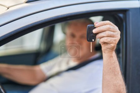 Téléchargez les photos : Moyen âge homme aux cheveux gris souriant confiant tenant la clé de nouvelle voiture à la rue - en image libre de droit