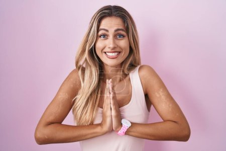 Photo for Young blonde woman standing over pink background praying with hands together asking for forgiveness smiling confident. - Royalty Free Image