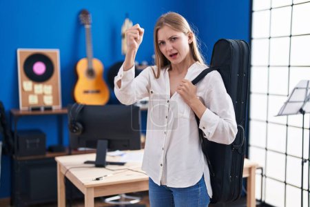 Photo for Young caucasian woman holding guitar case annoyed and frustrated shouting with anger, yelling crazy with anger and hand raised - Royalty Free Image