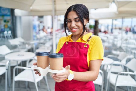Photo for Young beautiful arab woman waitress smiling confident holding take away coffee at coffee shop terrace - Royalty Free Image