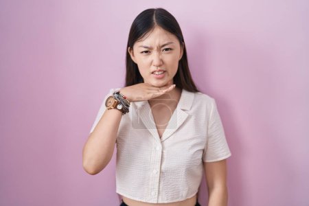Photo for Chinese young woman standing over pink background cutting throat with hand as knife, threaten aggression with furious violence - Royalty Free Image