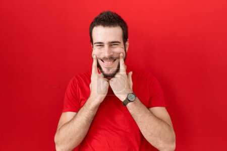 Téléchargez les photos : Jeune homme hispanique portant un t-shirt rouge décontracté souriant avec la bouche ouverte, les doigts pointant et forçant sourire joyeux - en image libre de droit