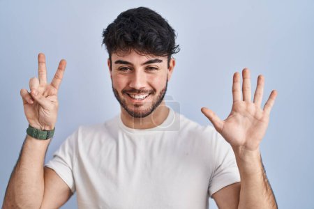 Téléchargez les photos : Hispanic man with beard standing over white background showing and pointing up with fingers number seven while smiling confident and happy. - en image libre de droit