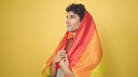 Téléchargez les photos : Jeune homme hispanique portant le drapeau arc-en-ciel avec une expression détendue sur fond jaune isolé - en image libre de droit