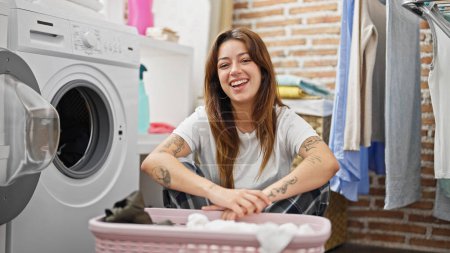 Photo for Young beautiful hispanic woman smiling confident leaning on basket with clothes at laundry room - Royalty Free Image