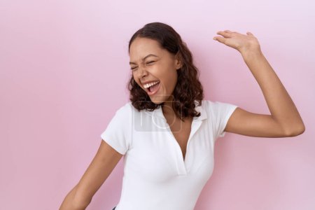 Foto de Young hispanic woman wearing casual white t shirt dancing happy and cheerful, smiling moving casual and confident listening to music - Imagen libre de derechos