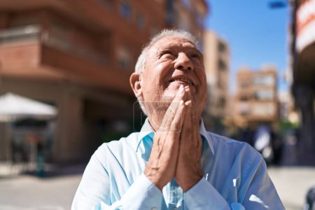 Téléchargez les photos : Moyen âge homme aux cheveux gris souriant confiant prier dans la rue - en image libre de droit