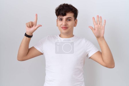 Téléchargez les photos : Jeune homme non binaire portant t-shirt blanc décontracté montrant et pointant vers le haut avec les doigts numéro sept tout en souriant confiant et heureux. - en image libre de droit