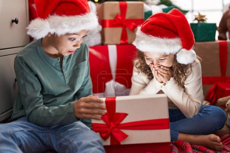 Foto de Dos niños desempacando regalo sentado en el suelo por el árbol de Navidad en casa - Imagen libre de derechos