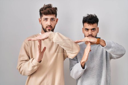 Téléchargez les photos : Jeune couple homosexuel debout sur fond blanc faisant un geste avec les mains, frustré et sérieux visage - en image libre de droit