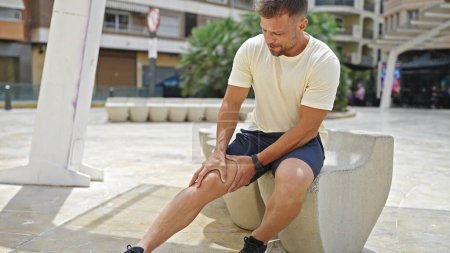 Téléchargez les photos : Jeune homme souffrant d'une blessure au genou assis sur un banc au parc - en image libre de droit