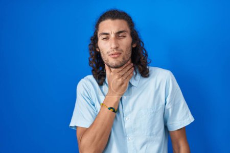 Photo for Young hispanic man standing over blue background touching painful neck, sore throat for flu, clod and infection - Royalty Free Image