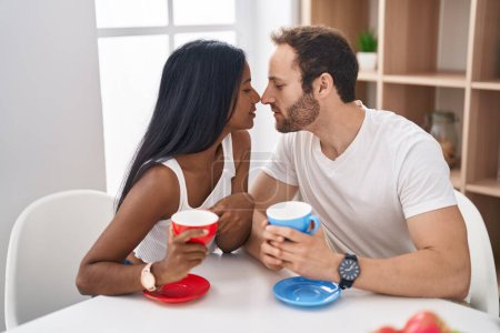 Téléchargez les photos : Homme et femme interracial couple boire du café assis sur canapé à la maison - en image libre de droit