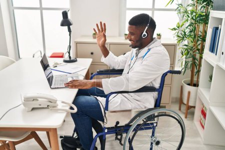 Photo for African american doctor man working on online appointment sitting on wheelchair looking positive and happy standing and smiling with a confident smile showing teeth - Royalty Free Image
