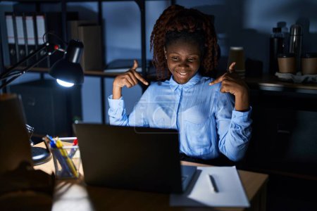 Photo for African woman working at the office at night looking confident with smile on face, pointing oneself with fingers proud and happy. - Royalty Free Image
