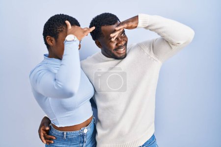 Téléchargez les photos : Jeune couple afro-américain debout sur fond bleu très heureux et souriant regardant loin avec la main sur la tête. concept de recherche. - en image libre de droit