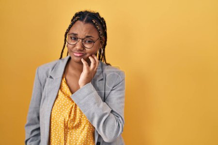 Photo for African american woman with braids standing over yellow background touching mouth with hand with painful expression because of toothache or dental illness on teeth. dentist - Royalty Free Image