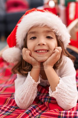 Foto de Adorable chica hispana sonriendo confiada tumbada en el suelo por el árbol de Navidad en casa - Imagen libre de derechos
