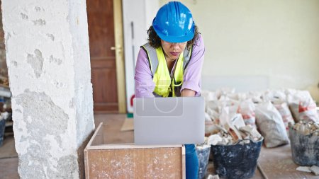 Téléchargez les photos : Jeune belle constructeur de femmes latines utilisant un ordinateur portable enlevant casque et lunettes sur le chantier de construction - en image libre de droit
