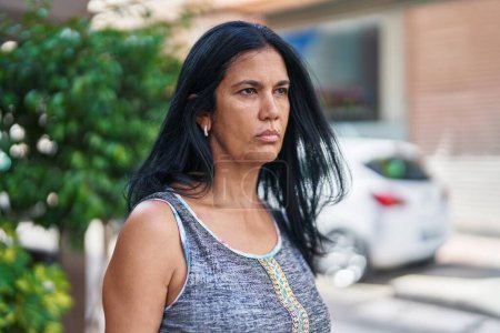 Téléchargez les photos : Moyen Age femme hispanique regardant vers le côté avec une expression sérieuse à la rue - en image libre de droit