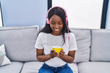 Téléchargez les photos : Jeune femme afro-américaine écoutant de la musique boire du café à la maison - en image libre de droit