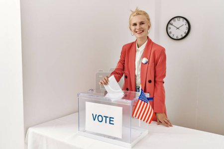 Foto de Joven mujer rubia presidente de mesa electoral poniendo votación en urnas en colegio electoral - Imagen libre de derechos