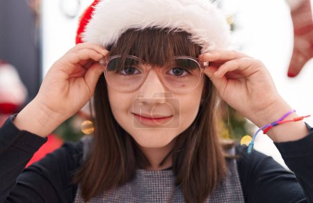 Téléchargez les photos : Adorable fille hispanique souriant confiant debout par arbre de Noël à la maison - en image libre de droit