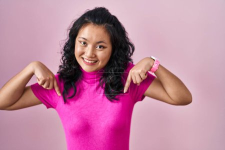 Foto de Young asian woman standing over pink background looking confident with smile on face, pointing oneself with fingers proud and happy. - Imagen libre de derechos