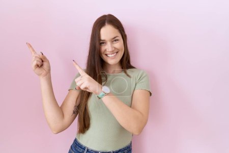 Photo for Beautiful brunette woman standing over pink background smiling and looking at the camera pointing with two hands and fingers to the side. - Royalty Free Image