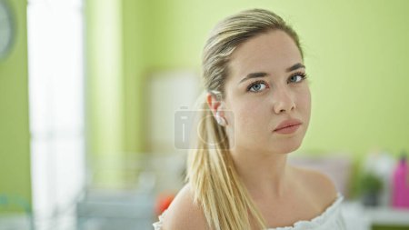 Téléchargez les photos : Jeune femme blonde écoutant de la musique avec un visage sérieux à la buanderie - en image libre de droit
