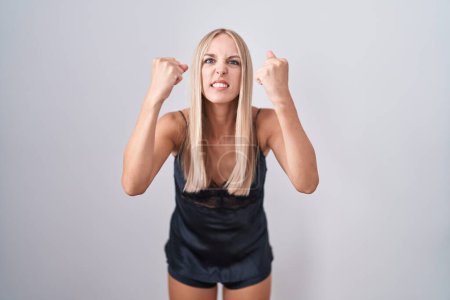 Photo for Young caucasian woman wearing nightgown angry and mad raising fists frustrated and furious while shouting with anger. rage and aggressive concept. - Royalty Free Image