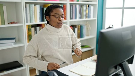 Téléchargez les photos : Étudiante afro-américaine utilisant le stylo comme batteur à l'université de la bibliothèque - en image libre de droit