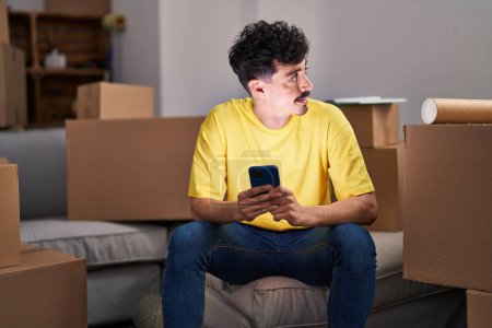 Téléchargez les photos : Young caucasian man using smartphone sitting on sofa at new home - en image libre de droit