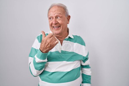 Photo for Senior man with grey hair standing over white background smiling with happy face looking and pointing to the side with thumb up. - Royalty Free Image