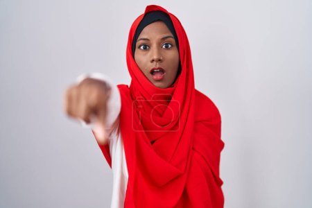 Téléchargez les photos : Jeune femme arabe portant traditionnel hijab islamique écharpe pointant avec le doigt surpris devant, bouche ouverte expression étonnante, quelque chose sur le devant - en image libre de droit