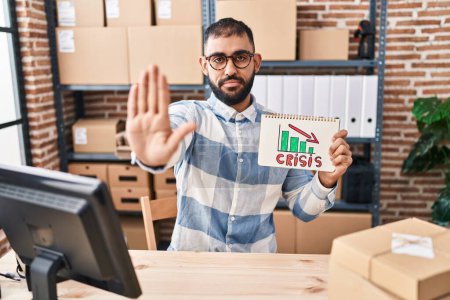 Photo for Middle east man with beard working at small business ecommerce holding crisis banner with open hand doing stop sign with serious and confident expression, defense gesture - Royalty Free Image