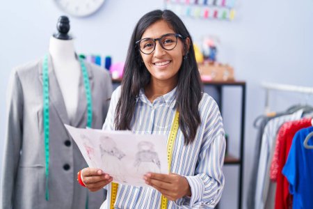 Téléchargez les photos : Jeune belle femme hispanique tailleur souriant conception de vêtements à la recherche confiante à l'usine de vêtements - en image libre de droit