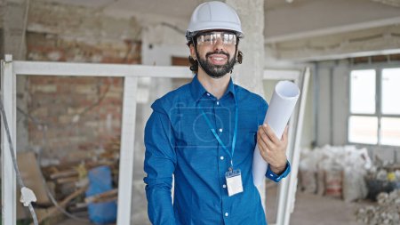 Photo for Young hispanic man architect smiling confident holding blueprints at construction site - Royalty Free Image
